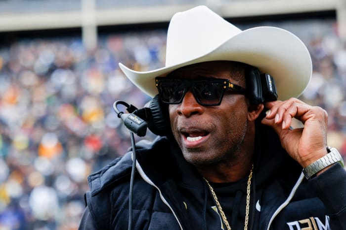Colorado football coach Deion Sanders wears a cowboy hat on the sidelines while talking into his headset.